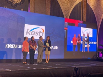 KOSTI receiving a plaque of recognition on stage